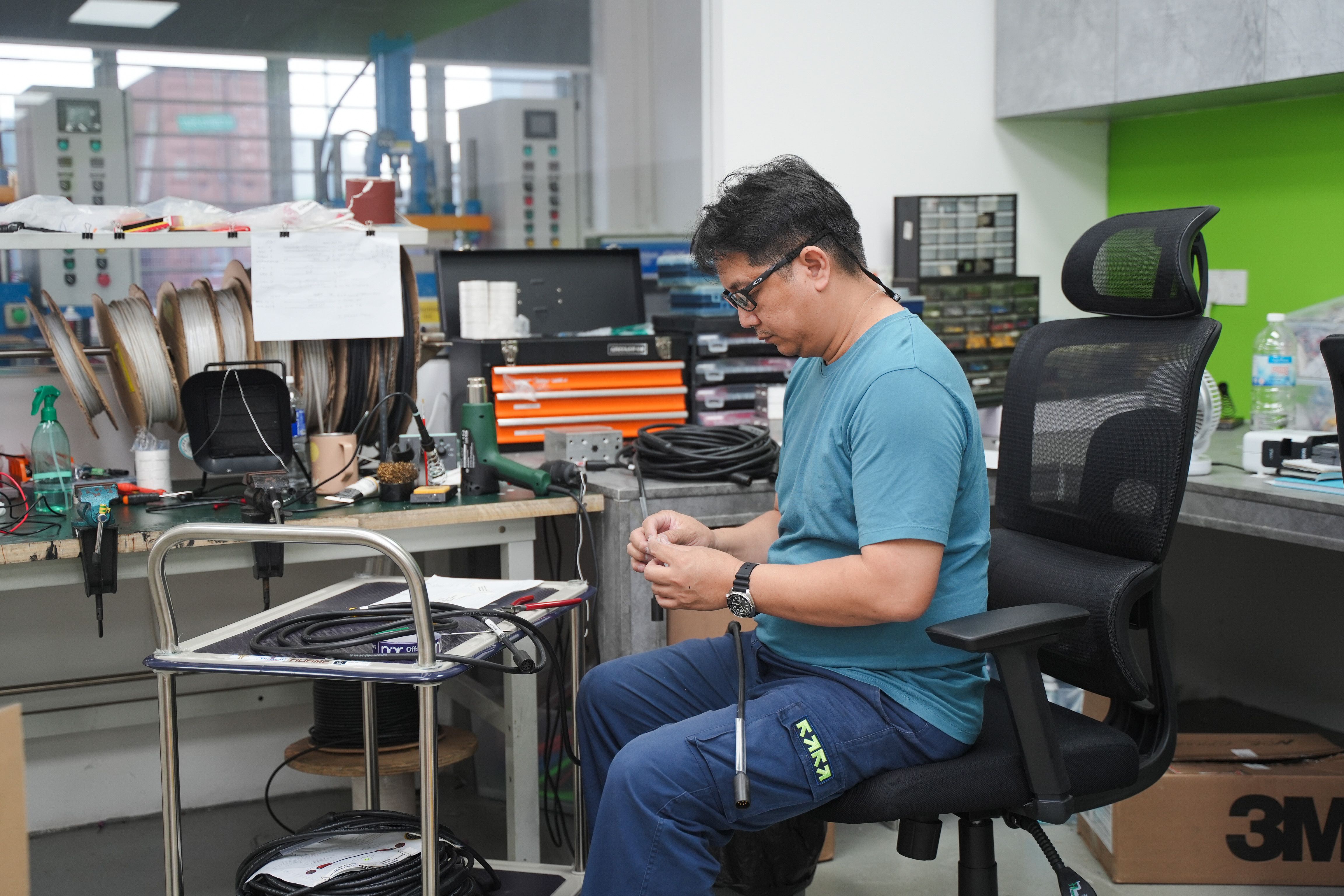 A man works with components at a workshop bench.