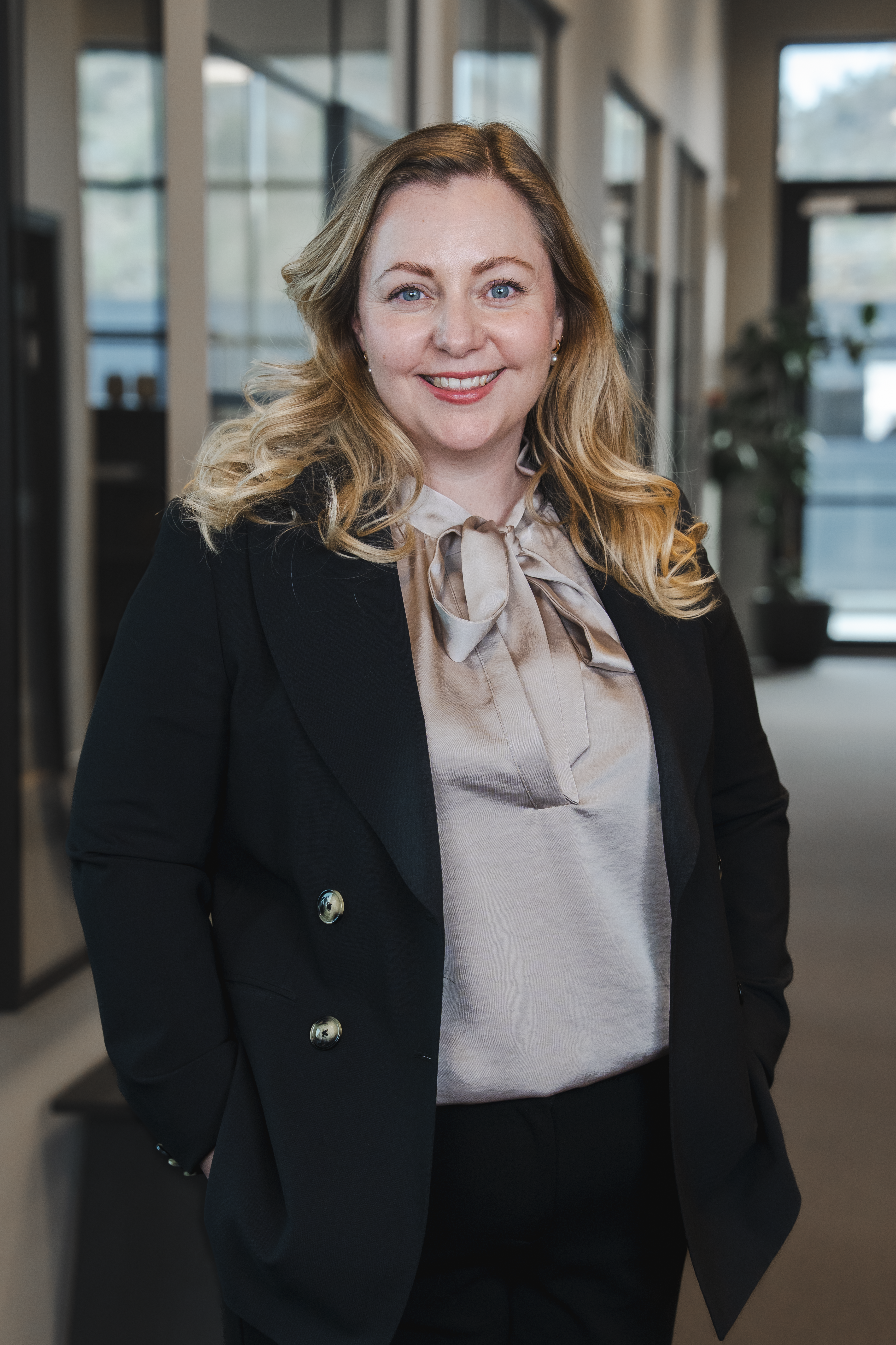 A smiling blonde woman in a black blazer and bow blouse.