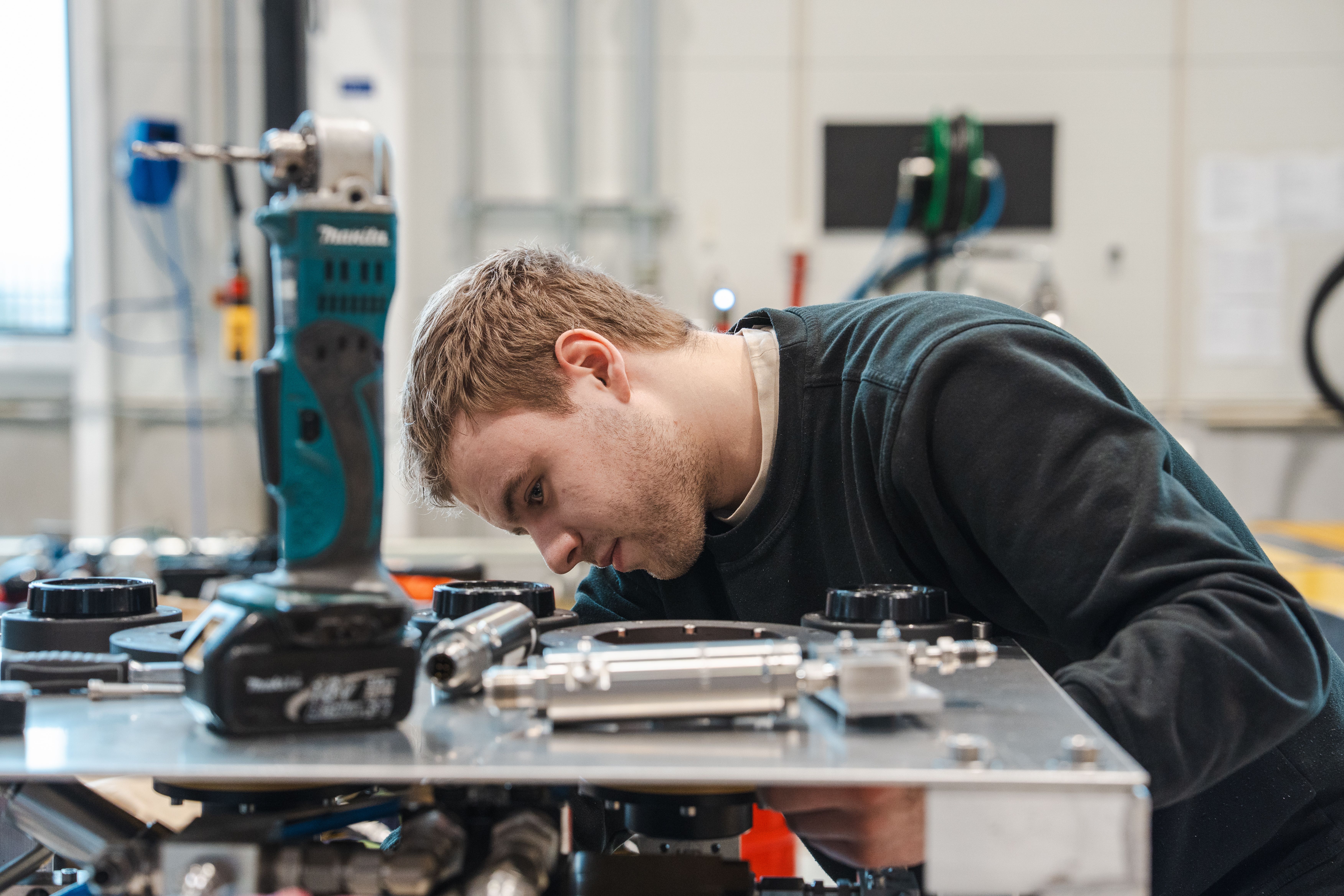 A young man intently working on mechanical equipment in a workshop.