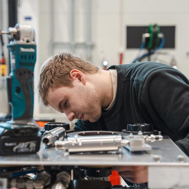 A young man intently working on mechanical equipment in a workshop.