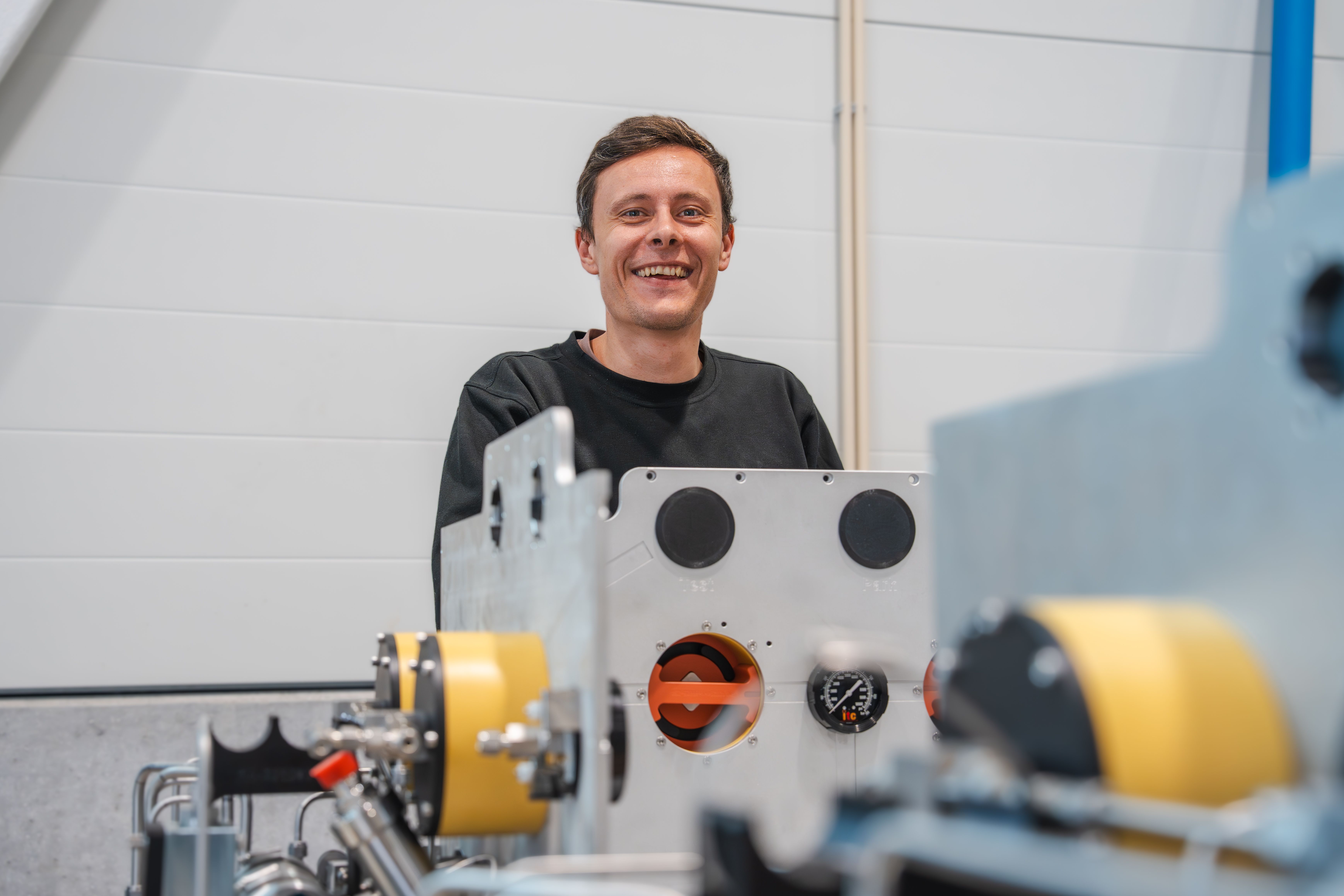 Smiling man behind industrial equipment with gauges.