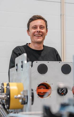 Smiling man behind industrial equipment with gauges.
