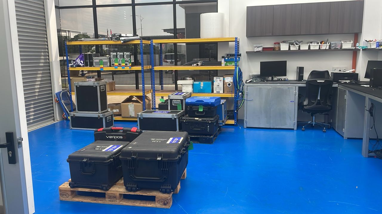 A room with a blue floor, black equipment cases, industrial shelving, and computer workstations.