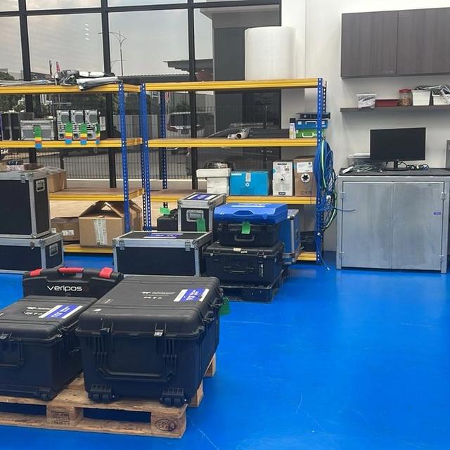 A room with a blue floor, black equipment cases, industrial shelving, and computer workstations.