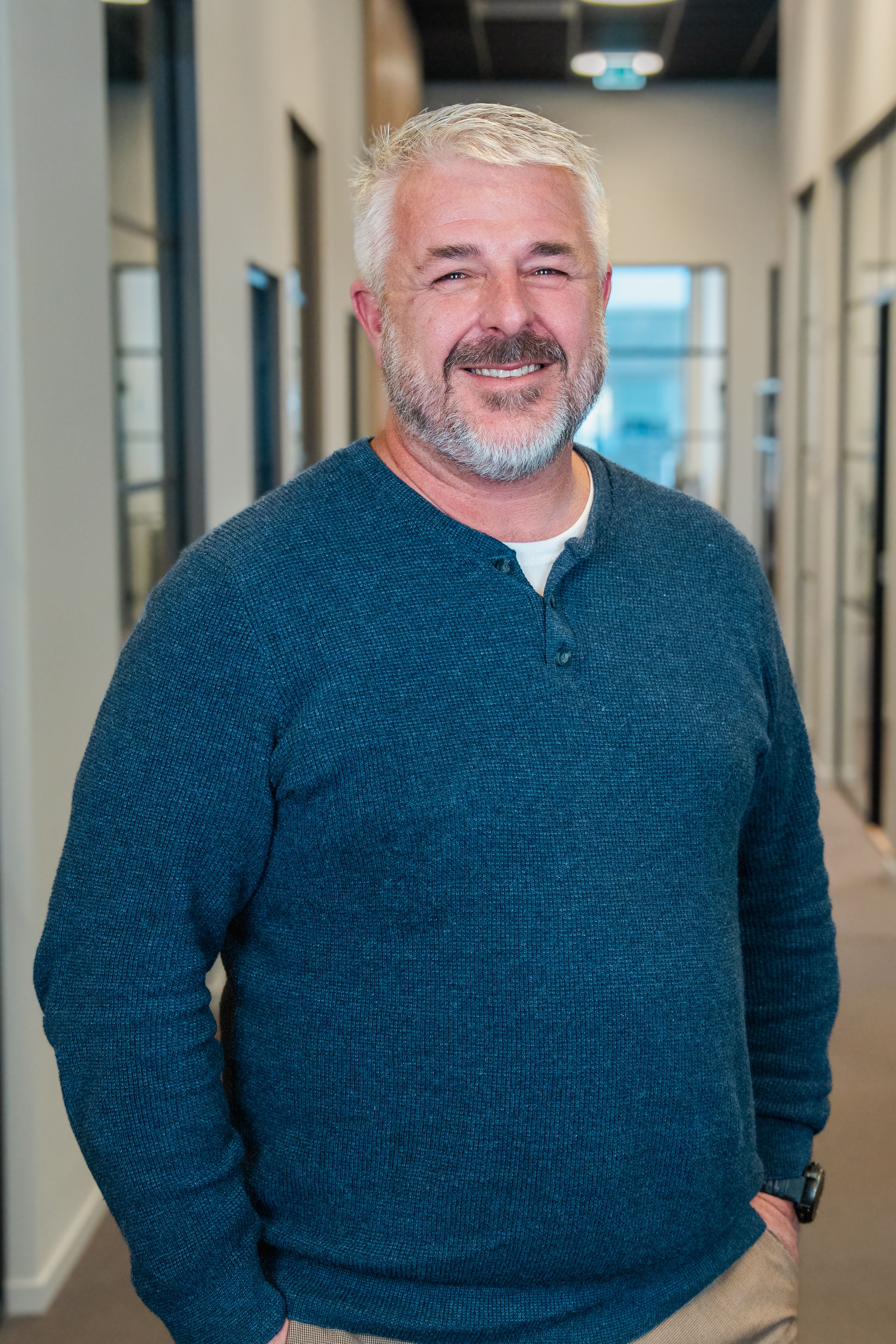 A smiling man with a gray beard wearing a blue long-sleeved shirt.