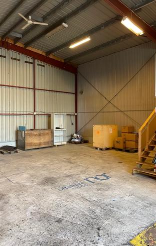A spacious warehouse interior with a high metal ceiling, concrete floor, wooden crates, stairs, and a "Norwegian Offshore Rental" logo.