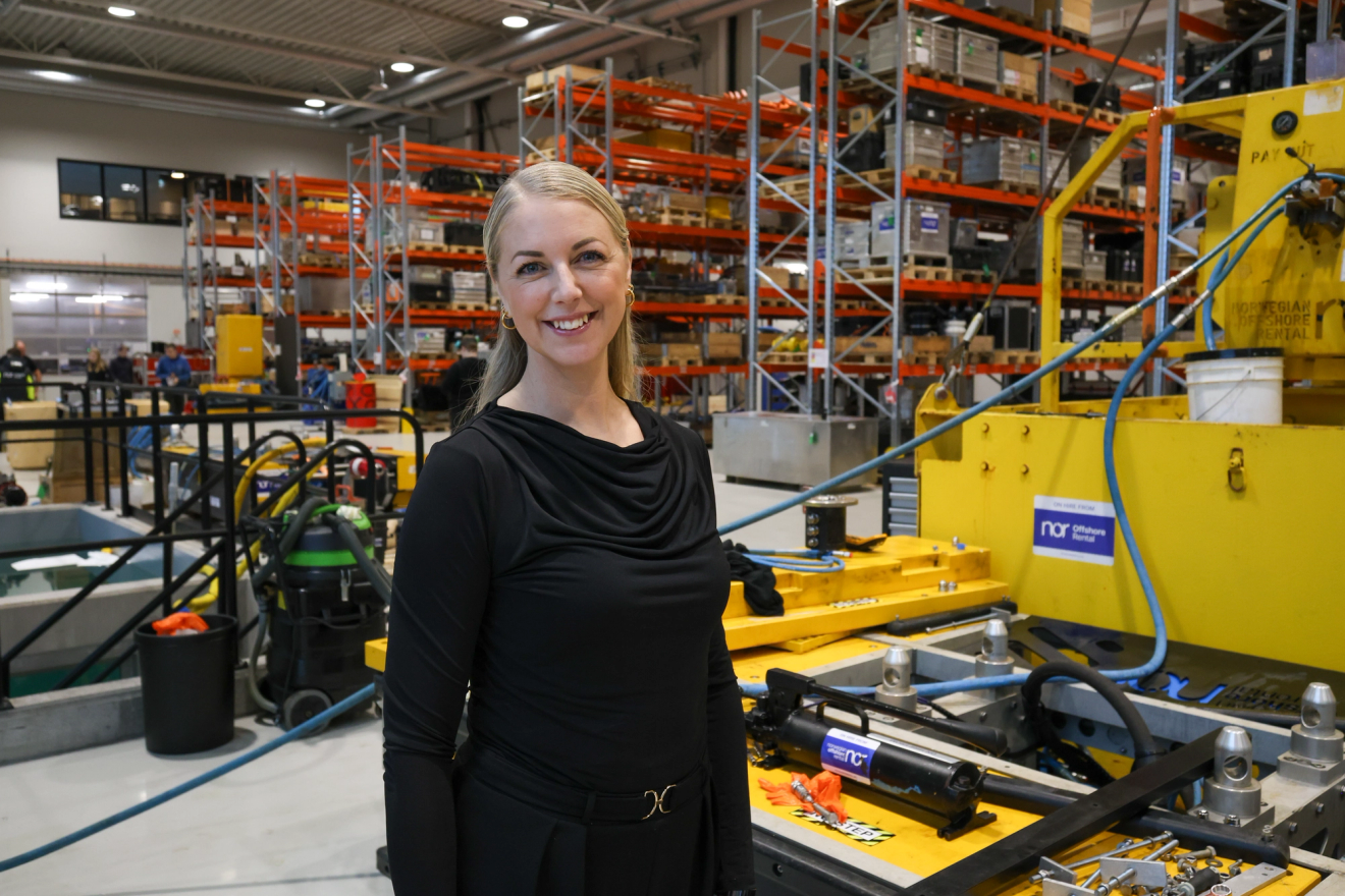 Smiling blonde woman in a black top stands in a warehouse.