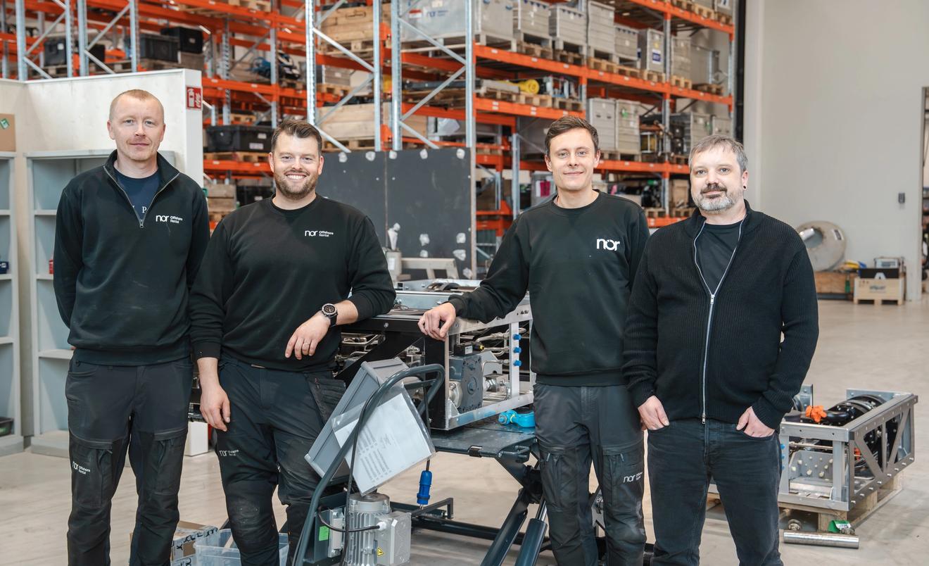 Four NOR team members standing in a workshop and warehouse environment with technical equipment and offshore project assemblies in the background.