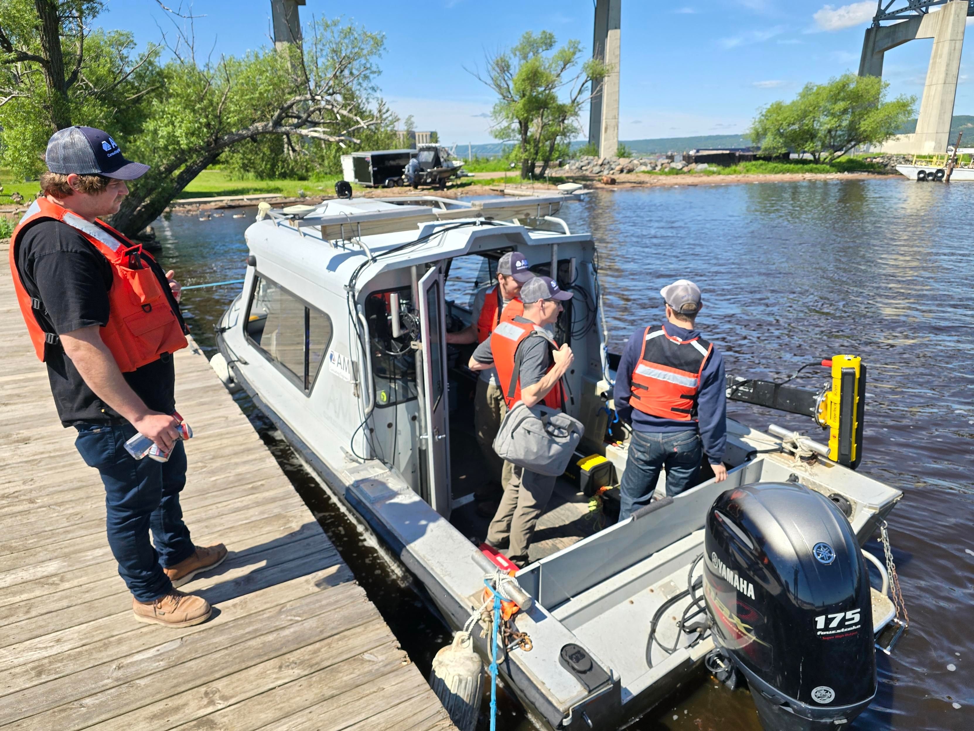 A team in life vests loads surveying equipment onto a boat docked on a sunny day.