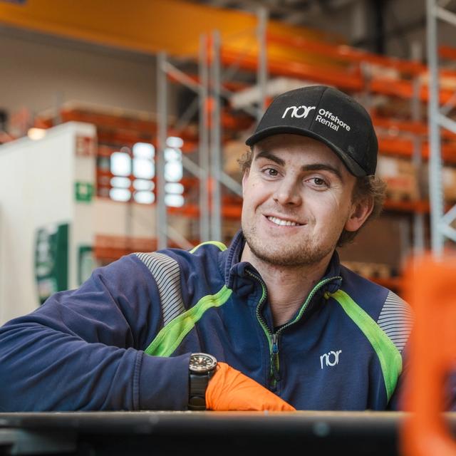 A smiling man wearing a "nor Offshore Rental" cap and uniform in an industrial setting.