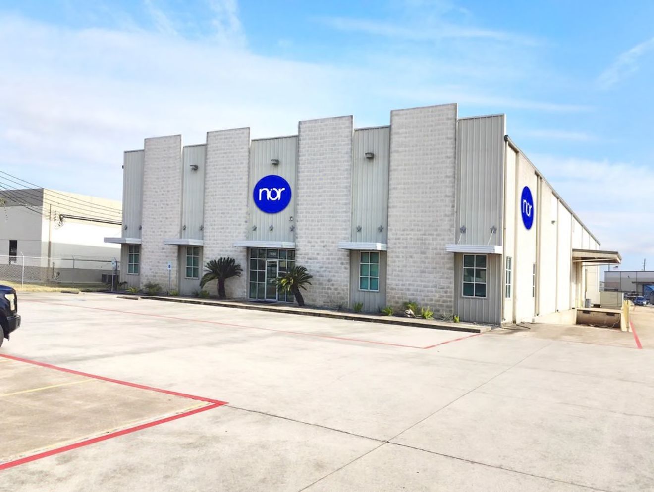 A white and grey commercial building with a blue "nor" logo, a parking lot, and a loading dock.