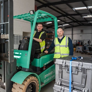 Two men in high-vis vests with a green forklift moving Sonardyne branded cases in a warehouse.