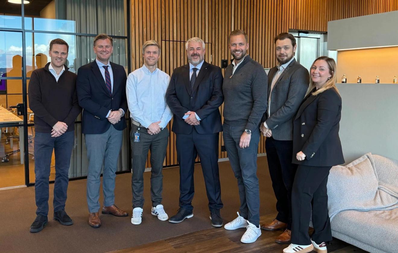Seven smiling professionals, five men and two women, standing in a modern office.