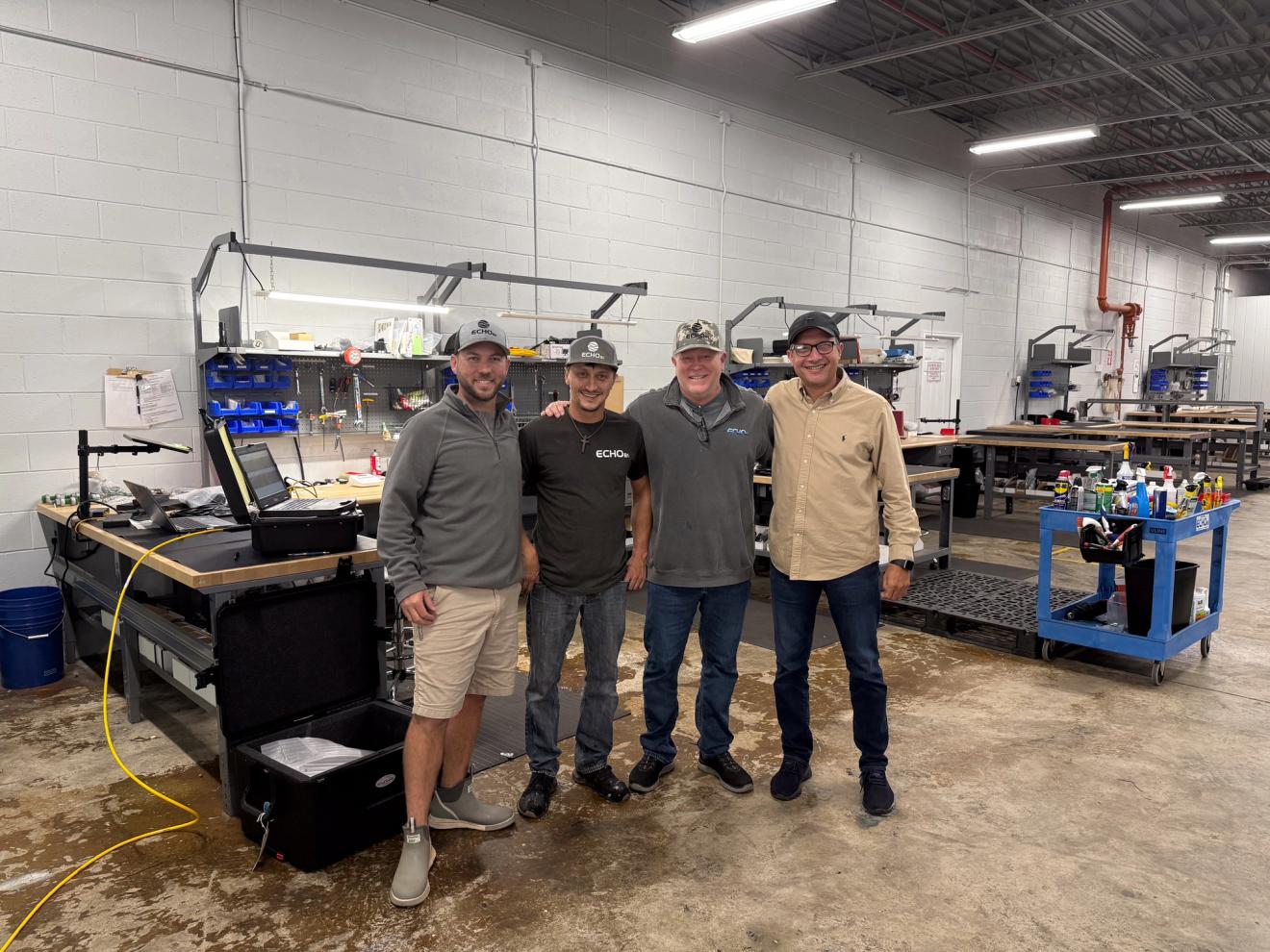 Four smiling men pose in a workshop.