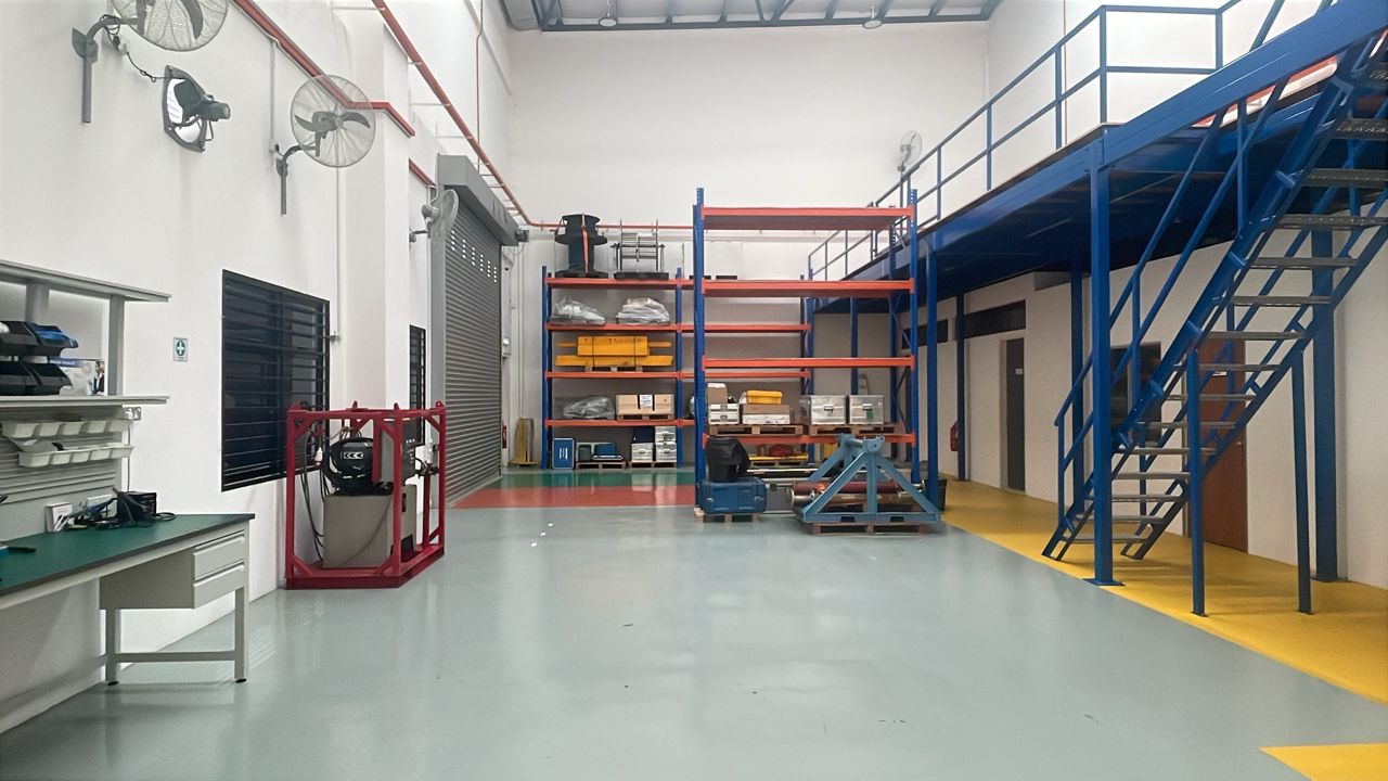 A clean industrial space featuring a blue mezzanine with stairs, storage racks, and a workbench.