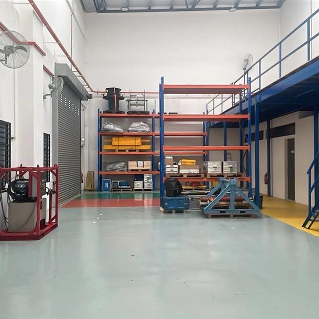 A clean industrial space featuring a blue mezzanine with stairs, storage racks, and a workbench.