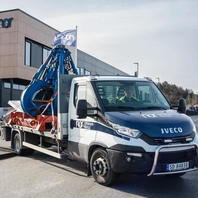 NOR Offshore branded Iveco truck carrying large industrial machinery in front of a building.
