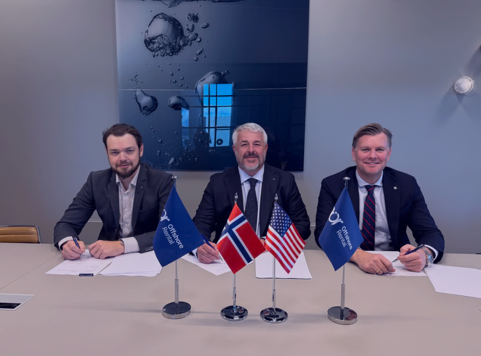 Three men in suits sit at a table with flags for Offshore Rental, Norway, and the USA, appearing to sign documents.