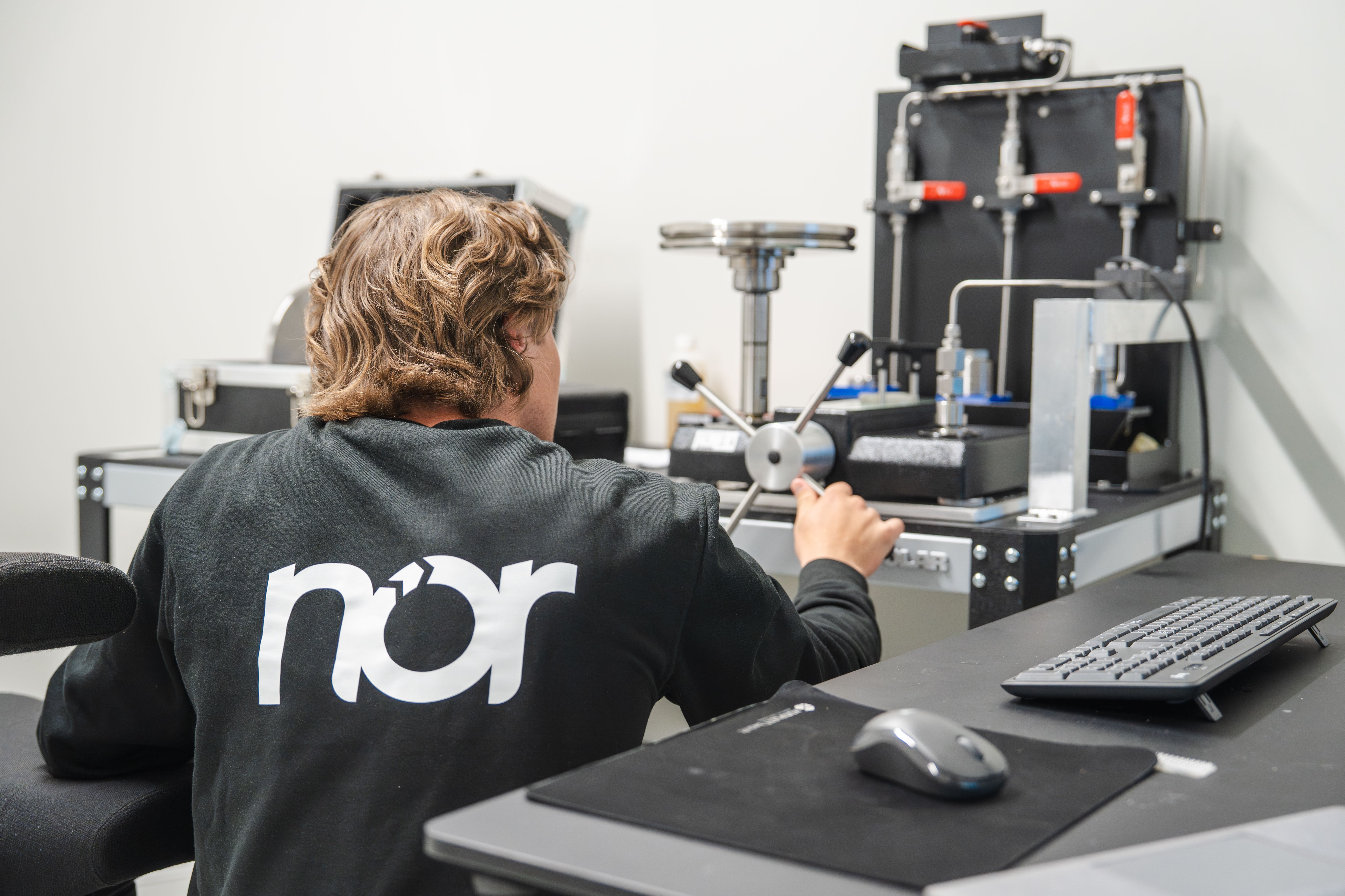 A person wearing a black sweatshirt with the "nor" logo on the back operates scientific equipment.