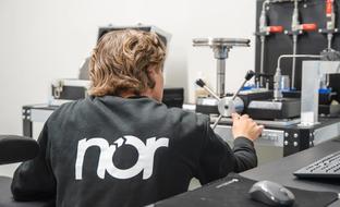 A person wearing a black sweatshirt with the "nor" logo on the back operates scientific equipment.