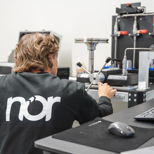 A person in a black "nor" sweatshirt operates lab equipment in calibration room.