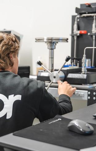 A person in a "nor" sweatshirt operates technical lab equipment.
