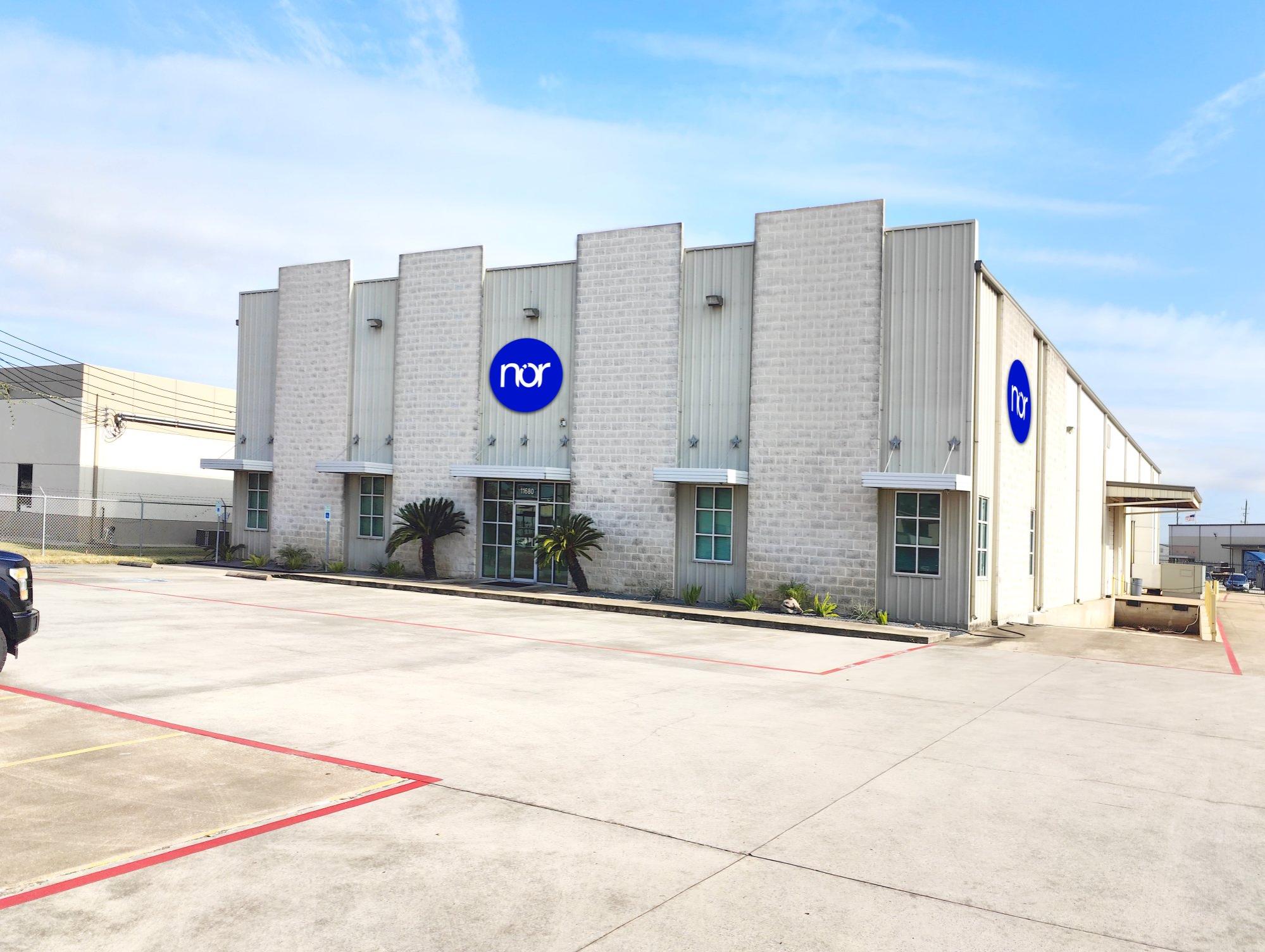 A modern industrial building with the "nor" logo on its facade, a parking lot, and a loading dock.