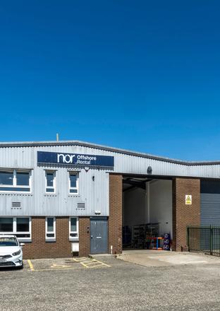 A gray industrial building with a "nor Offshore Rental" sign, two cars parked outside, and a clear blue sky.