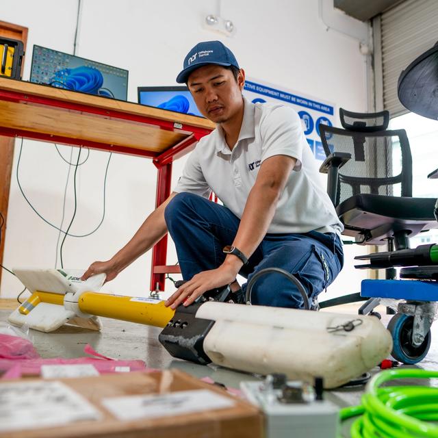 A man in a Nor Offshore Services uniform crouches, working on yellow and white oceanographic equipment on the floor.