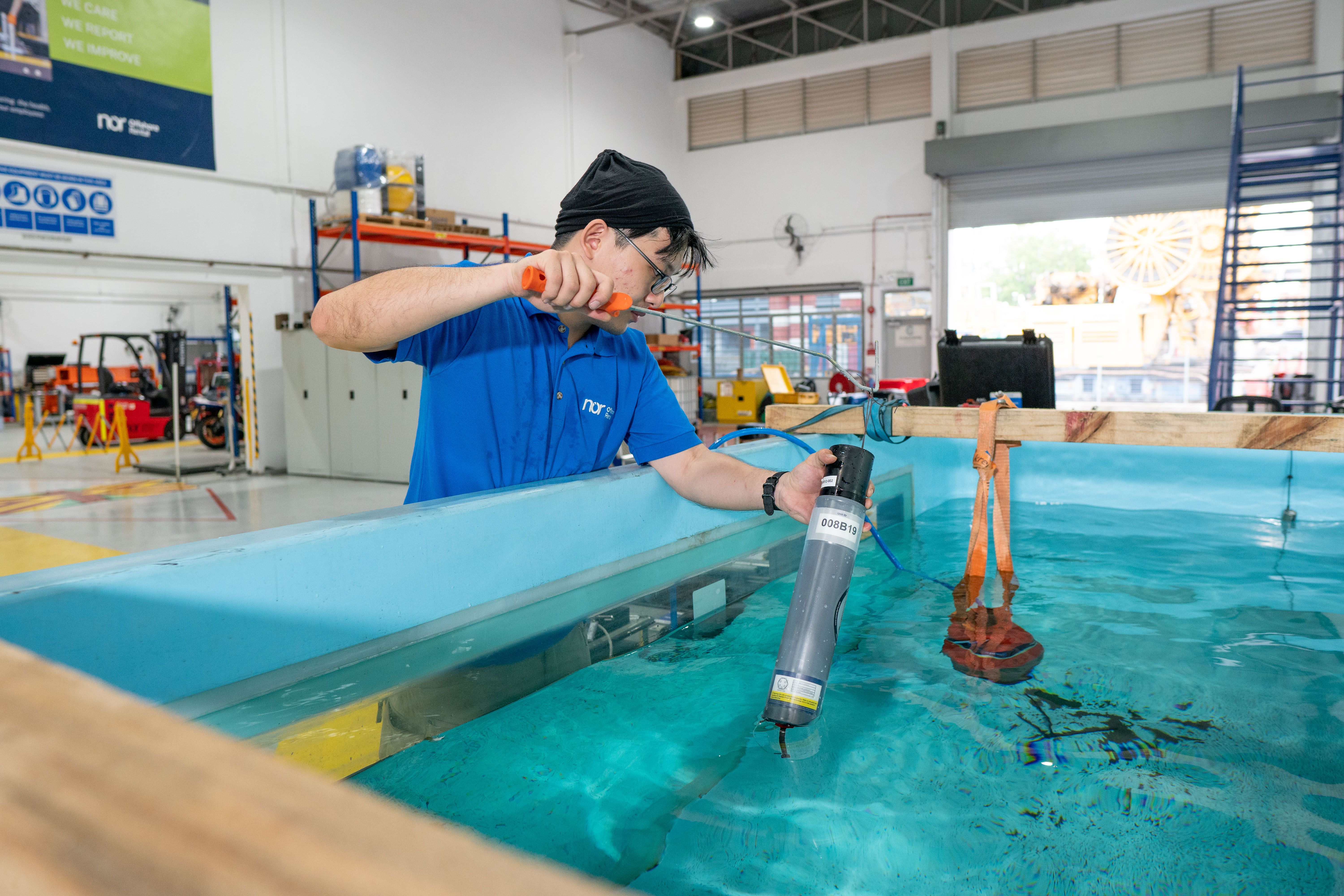 A person submerges a device into a large water tank in a lab.