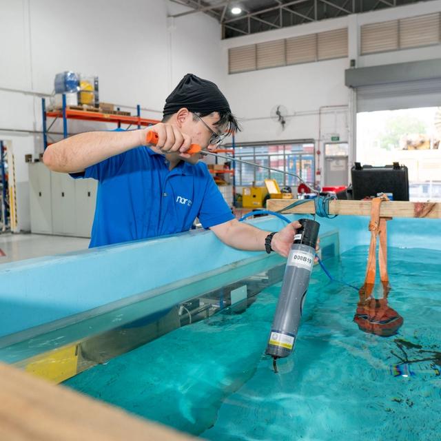 A person submerges a device into a large water tank in a lab.