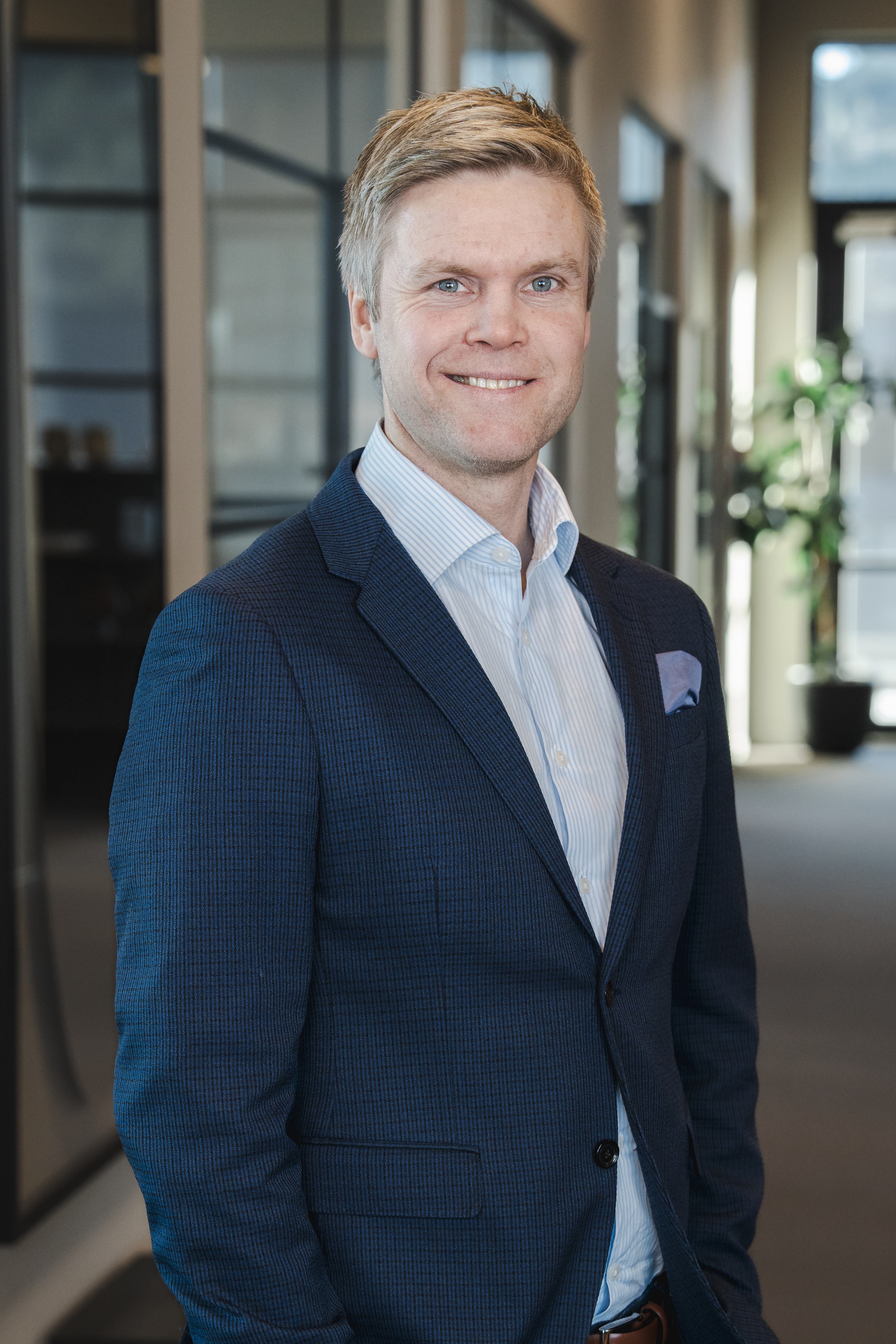 Smiling man with blond hair and blue eyes wearing a blue suit.