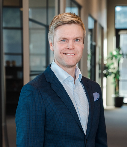 Smiling man with blond hair and blue eyes wearing a blue suit.
