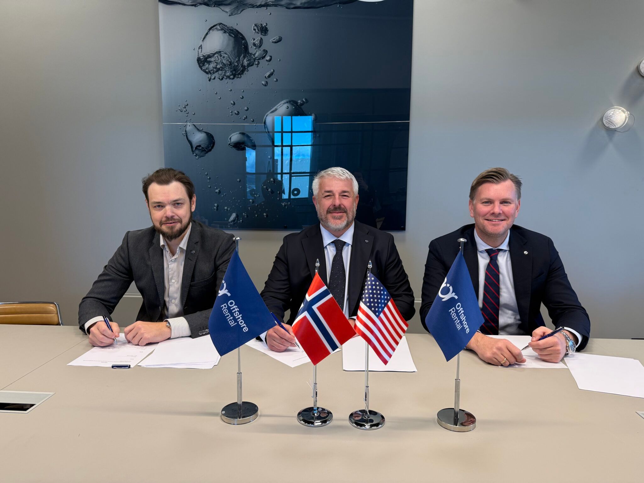 Three men in suits sign documents at a table with small flags of Norway, USA, and Offshore Rental.