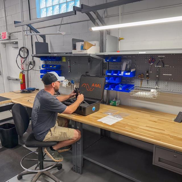 A man works on equipment from an open case at a workshop bench.