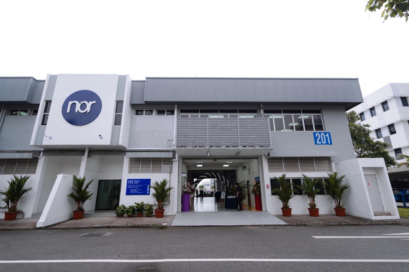 Modern grey and white building with a "nor" logo, the number 201, and an arched entrance.