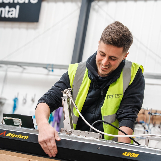 A smiling man in a high-visibility vest adjusts an EdgeTech 4205 survey device in a workshop.