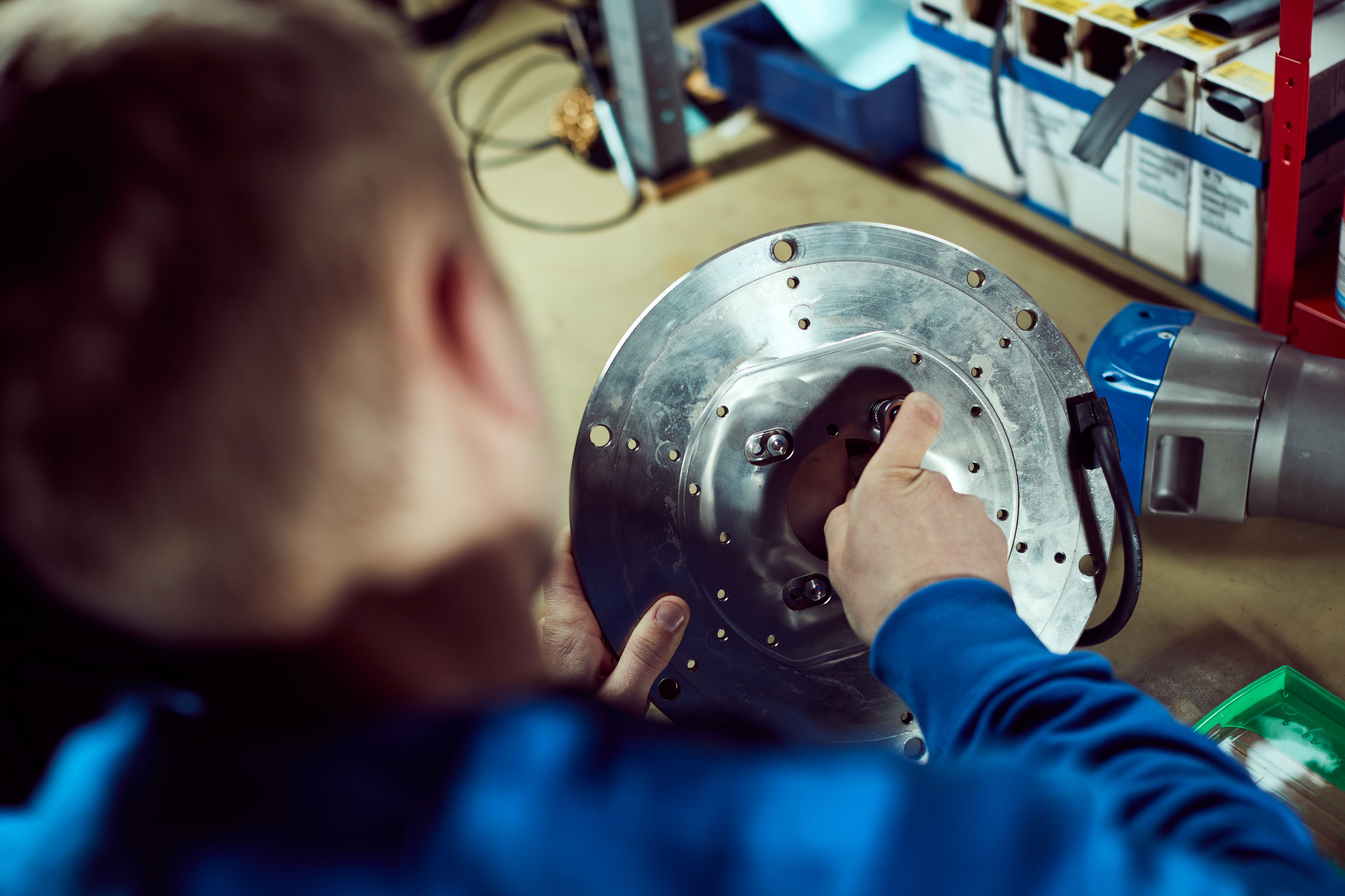 Person in a blue shirt assembling a circular metal component.