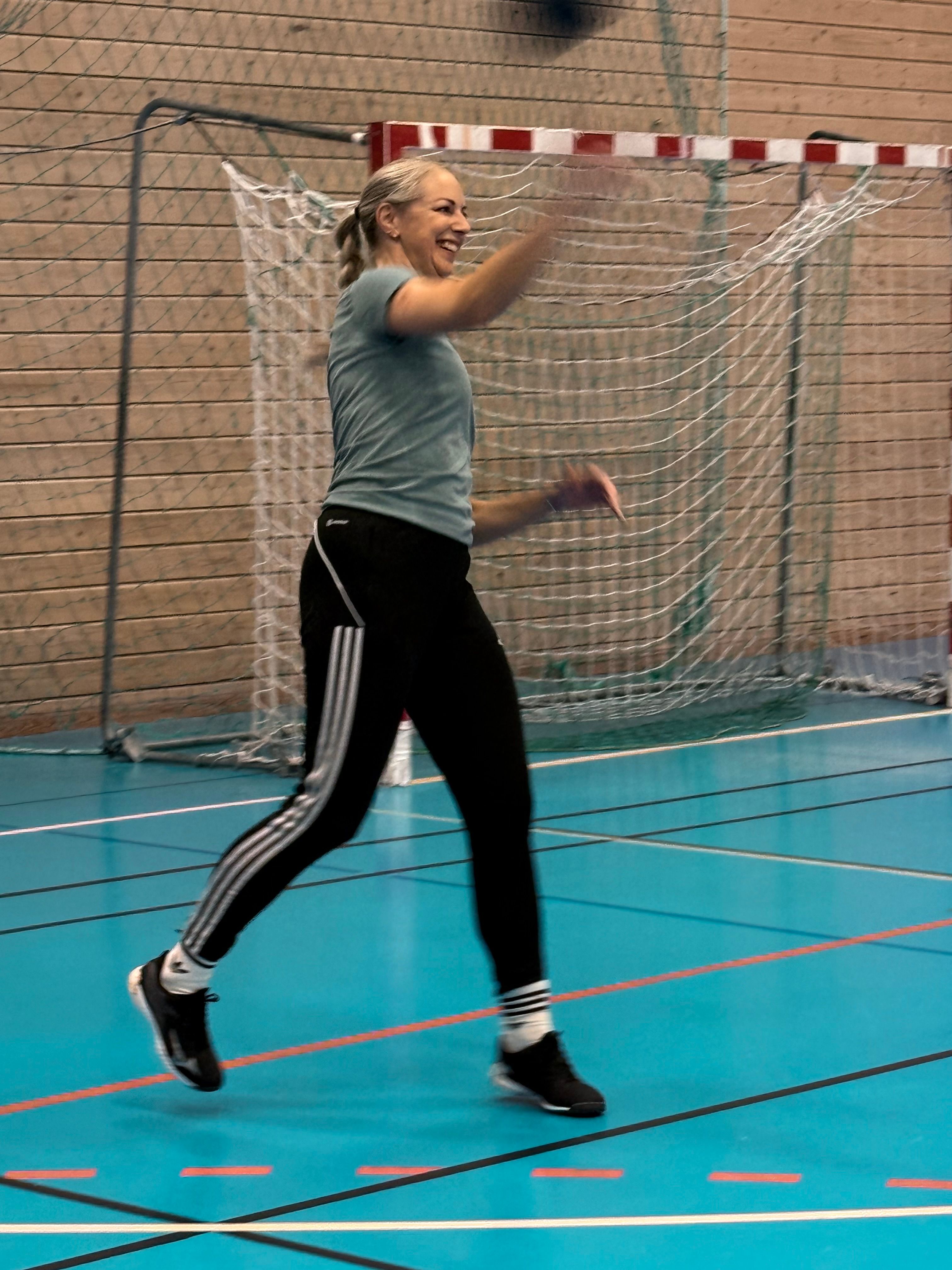 Smiling woman throwing a handball on a blue indoor court.