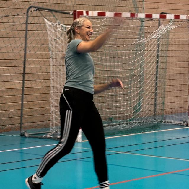 Smiling woman throwing a handball on a blue indoor court.