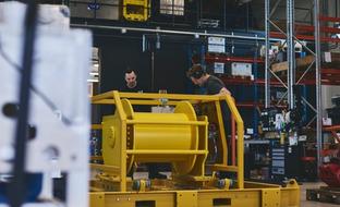 Two workers assembling a large yellow industrial machine in a workshop.