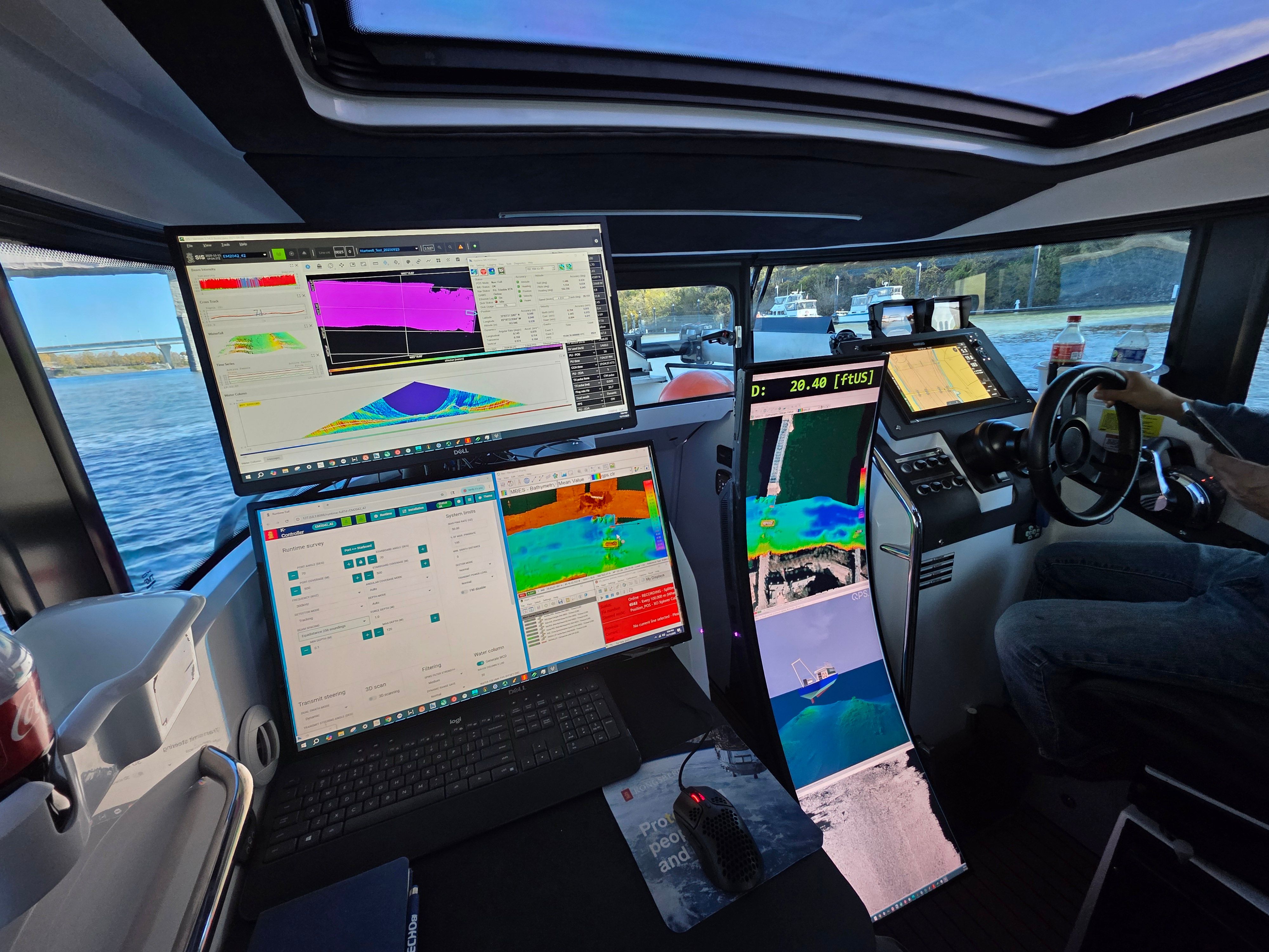Modern boat helm with a person steering, surrounded by multiple large displays showing sonar and navigation data.