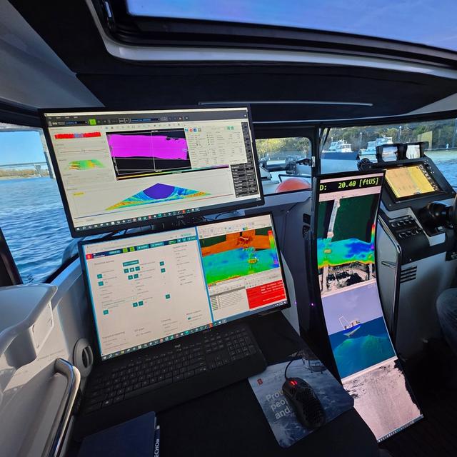 Modern boat helm with a person steering, surrounded by multiple large displays showing sonar and navigation data.