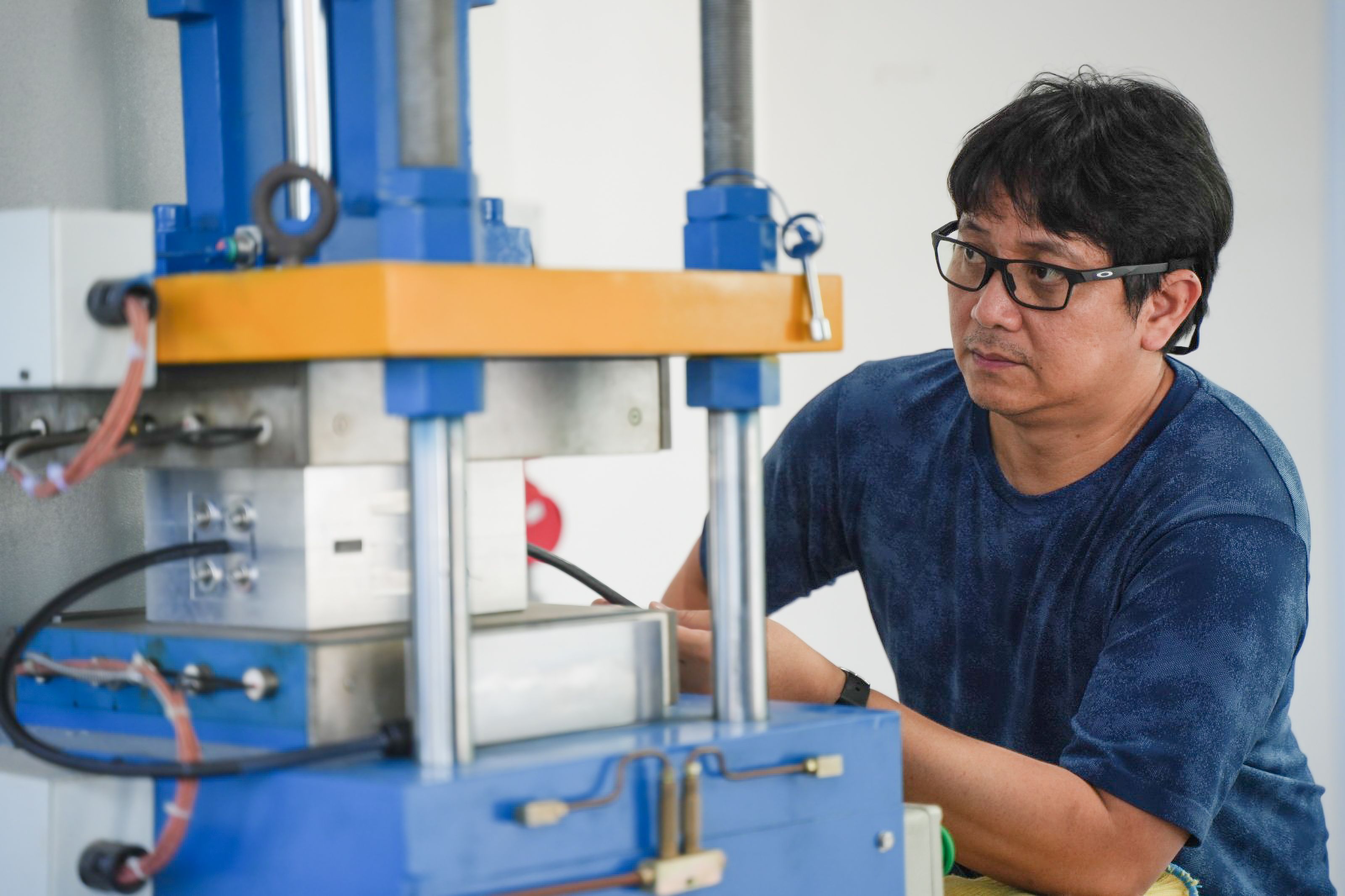 Man in glasses and a blue shirt looking at blue and yellow machinery.