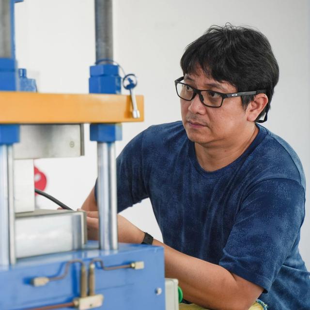 Man in glasses and a blue shirt looking at blue and yellow machinery.
