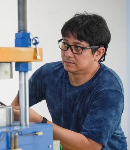 Man in glasses and blue shirt observing a large machine.