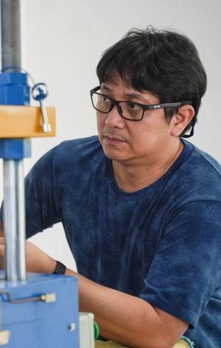 A man in glasses and a blue shirt looks intently at industrial machinery.