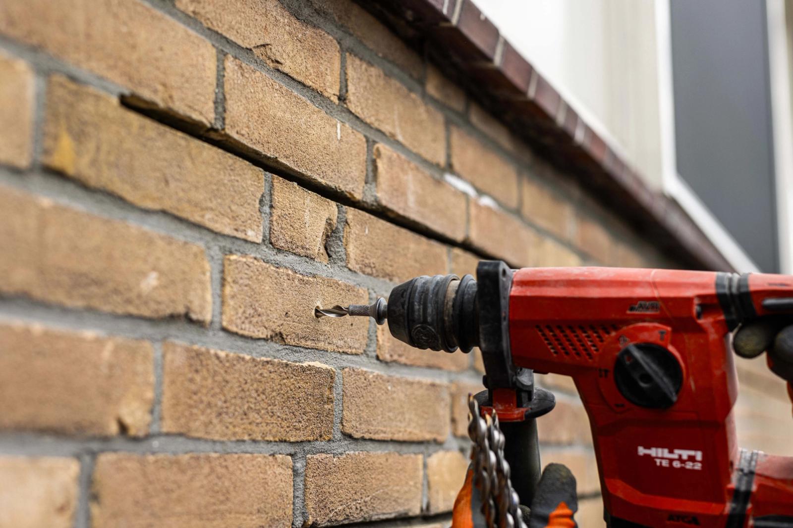 Vakman brengt een RVS renovatieanker aan in een bestaande bakstenen gevel