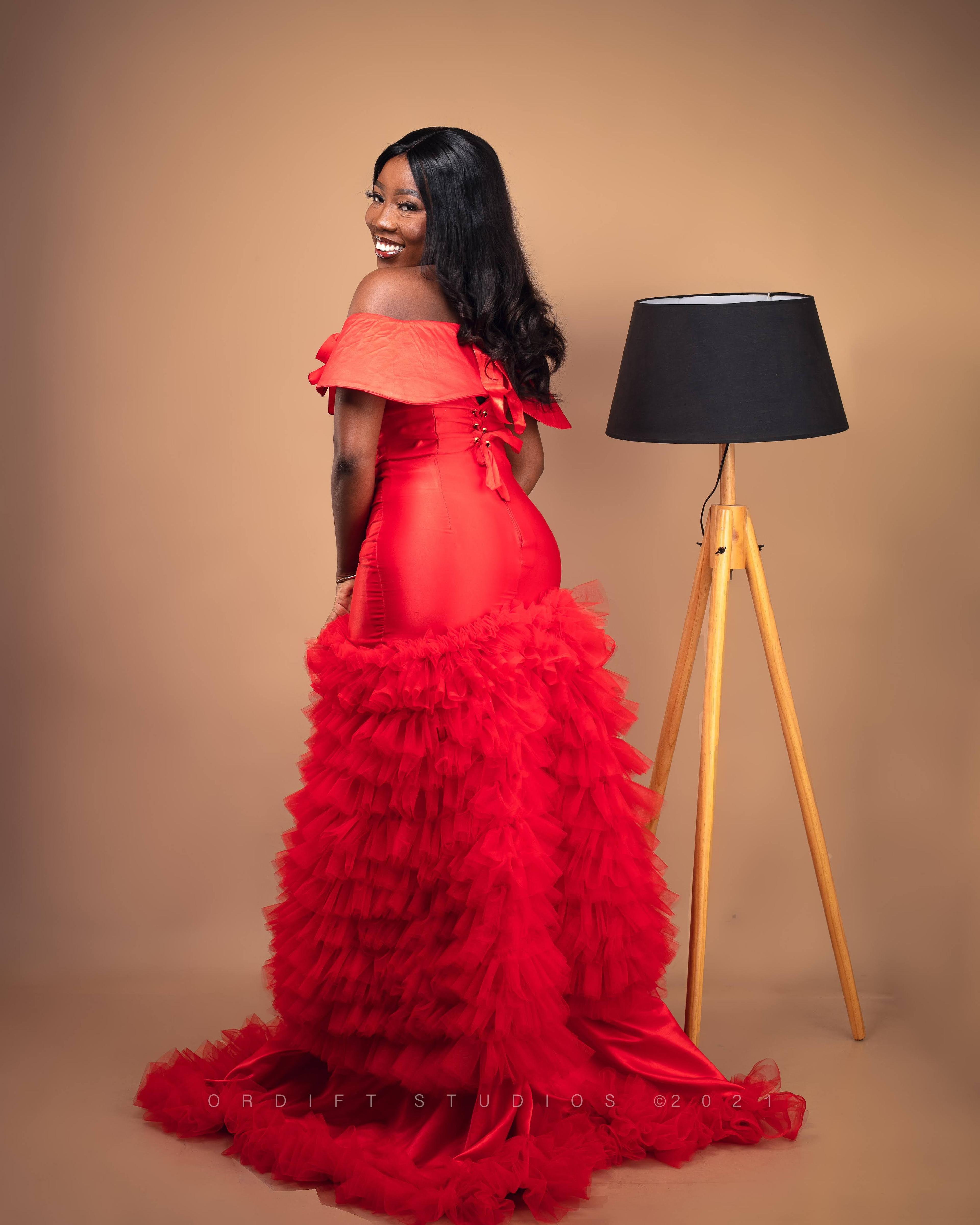 Model wearing a flowing red evening gown in a professional studio portrait.