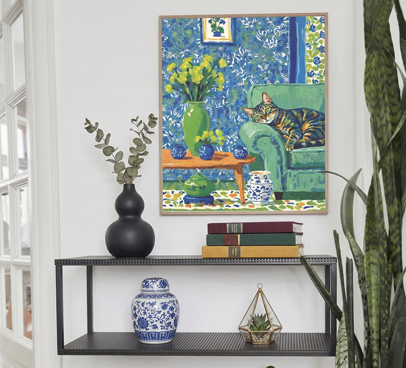 The Art of Doing Nothing impressionist pet portrait in cool blue and green tones hanging above a black console table with blue-and-white ceramic vase and green plants